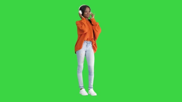 緑の画面で音楽を楽しむヘッドフォンを身に着けている若いアフリカの女性, Chroma Key. — ストック動画