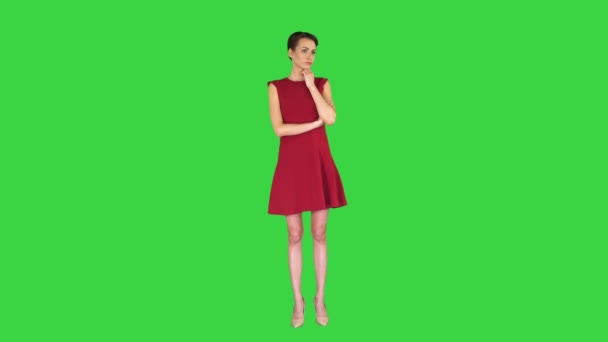 Atractiva mujer joven en vestido rojo de pie y escuchando a alguien hablar en una pantalla verde, Chroma Key . — Vídeo de stock