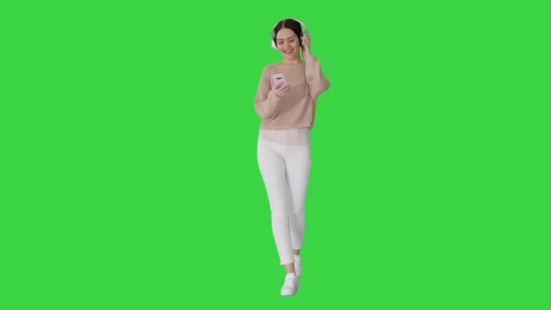 Schöne Frau, die spazieren geht, während sie Musik auf einem grünen Bildschirm hört, Chroma Key. — Stockvideo