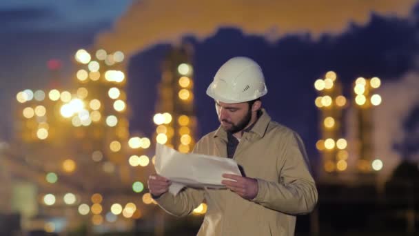 Ingeniero joven con impresión azul en el fondo de la fábrica de aceite por la noche . — Vídeos de Stock