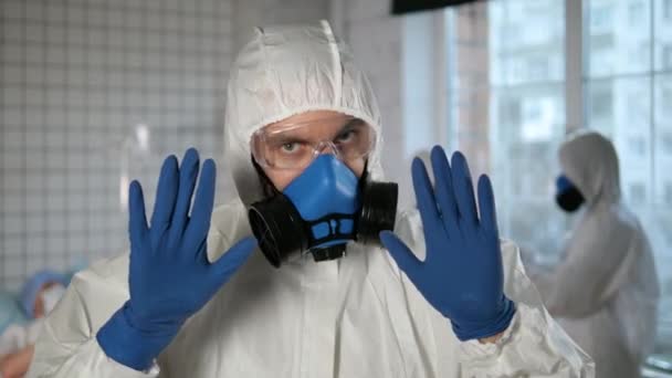 De dokter draagt een masker en een beschermend pak en maakt een stop gebaar naar de camera. Maak je geen zorgen. Ziekenhuis. — Stockvideo