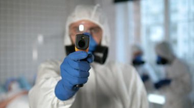 Doktor koruyucu giysi, kameranın arkasındaki kişinin sıcaklığını ölçmek için pirometre kullanıyor..