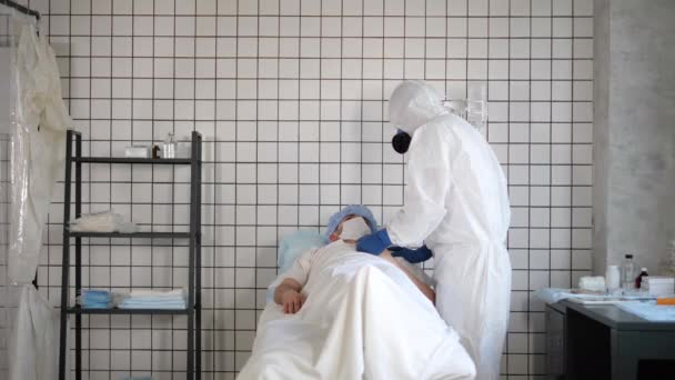 Γιατρός στο Hazmat Sterile κοστούμι κρατώντας το χέρι του ανδρικού ασθενούς προσπαθεί να τον εμπνεύσει. — Αρχείο Βίντεο