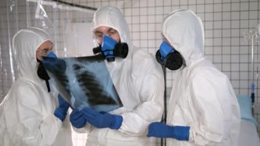 Koruyucu giysiler içinde laboratuvar doktorları akciğer röntgenine bakıyor..