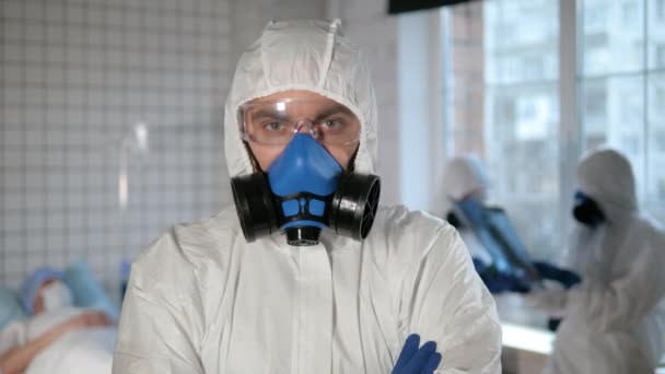 Confident man in a biohazard suit folds hir arms and shows elements of his protection suit. — Stock Video