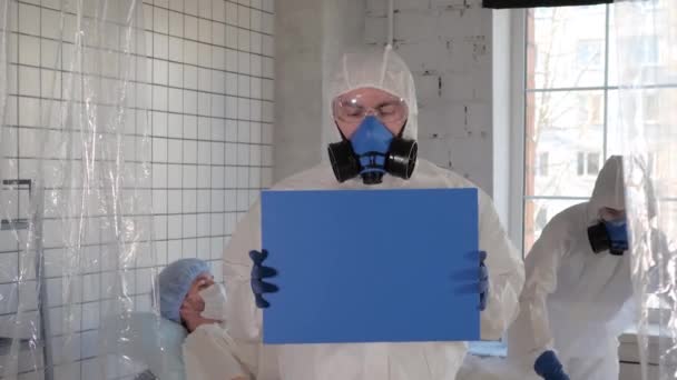 Dokter in de beademing toont blanco boord in een ziekenhuis. Besmette patiënt in quarantaine liggend in bed. — Stockvideo