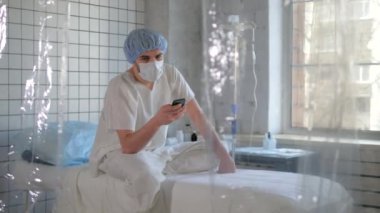Maskeli yalnız bir adam hastanede telefonunu kullanıyor..