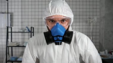 Koruyucu kıyafetli deli doktor kameraya bakıyor ve derin nefes alıyor..