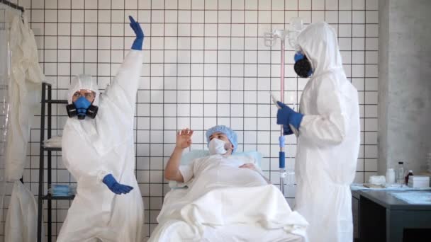 Dokter in beschermende pak dansen terwijl de patiënt ligt in het bed zich slecht voelen. — Stockvideo