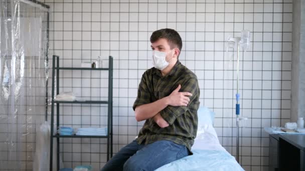 Jeune homme portant un masque de protection assis seul dans la chambre de l'hôpital en attendant les résultats des tests, isolement du coronavirus . — Video