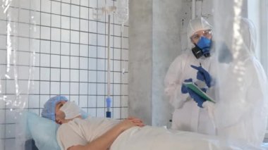 Koruyucu giysili ve maskeli doktorlar hasta adamı inceliyor..