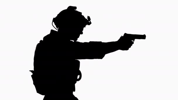 Silhouette Ein Soldat der Spezialeinheit mit einem Helm auf dem Kopf geht und schießt aus einer Handfeuerwaffe. — Stockvideo