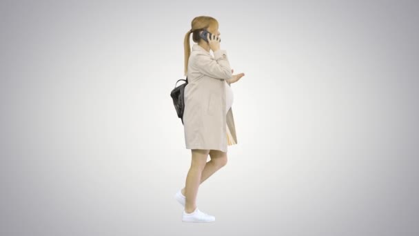 Pregnant woman with backpack walking and talking on the phone on gradient background. — Stock Video