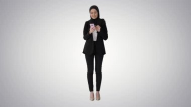 Türban takan genç müslüman kadın eğimli arka planda akıllı telefon kullanarak yürüyor.