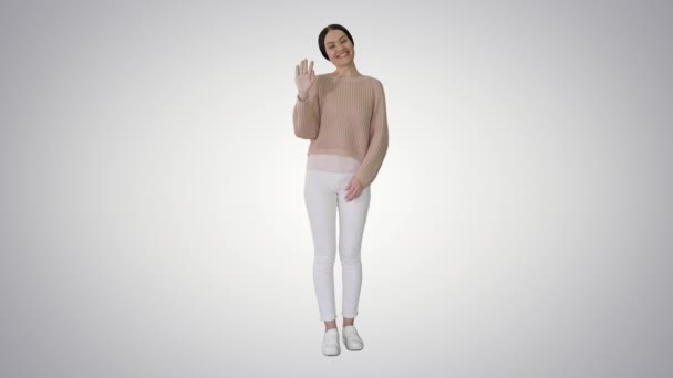 Šťastná mladá žena mává rukou, aby vás přivítala na skloněném pozadí. — Stock video