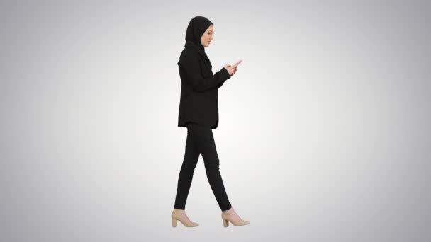 Perempuan dalam hijab menggunakan ponsel berjalan pada latar belakang gradien. — Stok Video