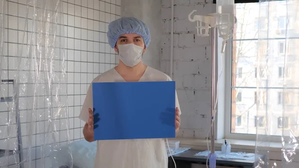 Junge männliche Patientin mit medizinischer Schutzmaske in einem Krankenhaus zeigt vor laufender Kamera leere Tafeln. — Stockfoto