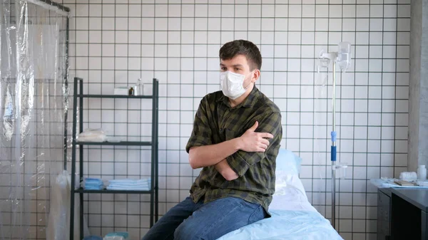 Hombre joven con máscara protectora sentado solo en la cámara del hospital esperando los resultados de las pruebas, aislamiento del coronavirus . —  Fotos de Stock