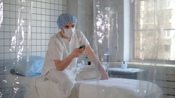 Isolated person in madical mask using his phone in a hospital.