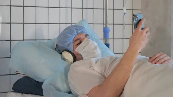 Młody pacjent leży w łóżku w szpitalu i słucha muzyki za pomocą słuchawek. — Zdjęcie stockowe