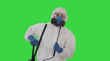 Kişisel koruyucu giysi, eldiven, maske ve yüz kalkanı takmış bir adam yeşil ekranda dezenfekte etmeye hazır..