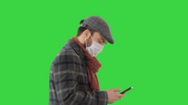 Tıbbi maskeli şık bir adam yürüyor ve yeşil ekranda akıllı telefon kullanıyor, Chroma Key..