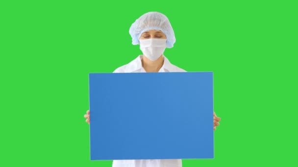 Woman doctor in a mask holding an empty board on a Green Screen, Chroma Key. — Stock Video