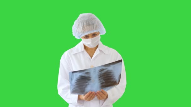 Vrouwelijke arts met medisch masker kijken naar röntgenfoto op een groen scherm, Chroma Key. — Stockvideo