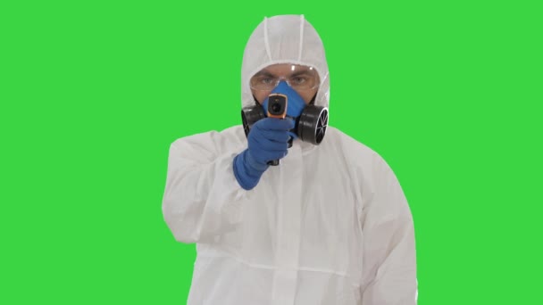 Man arts in beschermende pak met een digitale infrarood thermometer wijzen met het naar de camera op een groen scherm, Chroma Key. — Stockvideo