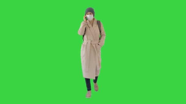 Ung kvinna i skyddsmask promenader och prata med mobiltelefon på en grön skärm, Chroma Key. — Stockvideo