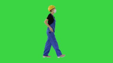 Siyah şapkalı ve tıbbi maskeli genç bir kadın yeşil ekranda yürüyor, Chroma Key.