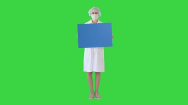 Maskeli genç bayan doktor yeşil ekranda boş bir pano tutuyor, Chroma Key..