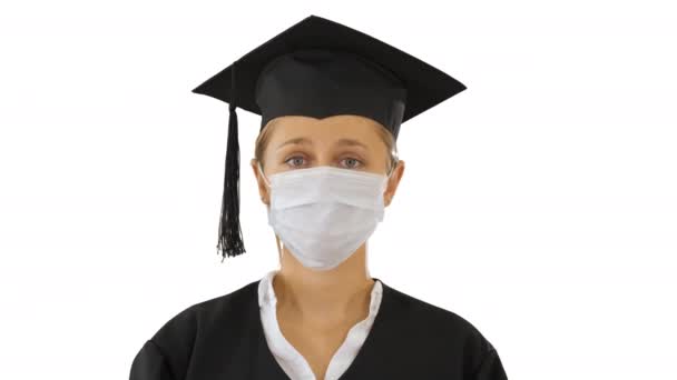 Afgestudeerde student dame in een medisch masker op zoek naar camera op witte achtergrond. — Stockvideo