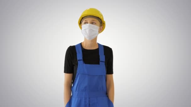 Young woman in yellow hardhat and in medical mask walking on gradient background. — Stock Video