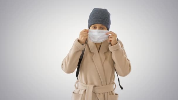 Blond vrouw lopen en zetten gezichtsbescherming op in preventie voor coronavirus covid 19 op gradiënt achtergrond. — Stockvideo