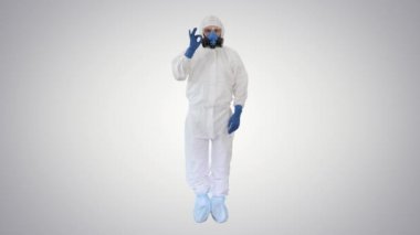 Koruyucu koruyucu giysi giyen doktor arka plandaki kameraya işaret ve baş parmak gösteriyor..