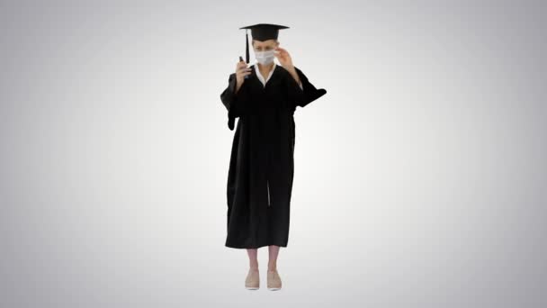 Φοιτητής αποφοίτησης με ιατρική μάσκα χρησιμοποιώντας απολυμαντικό σε βαθμιδωτό φόντο. — Αρχείο Βίντεο