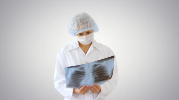 Kobieta lekarz noszący maskę medyczną patrząc na obraz rentgenowski na tle gradientowym. — Wideo stockowe