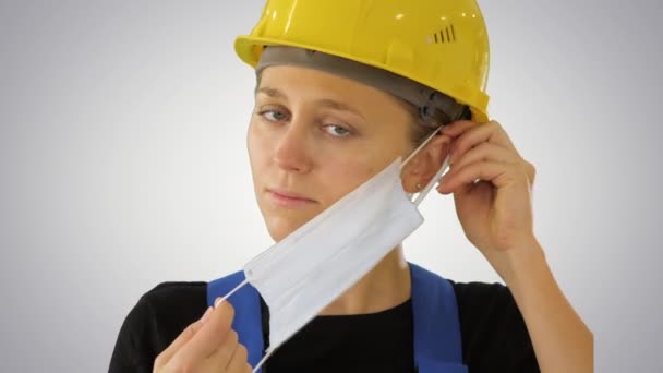 Trabalhadora da construção no capacete de segurança colocando máscara médica em fundo gradiente . — Vídeo de Stock