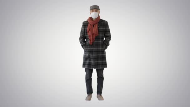 Uomo in stile inglese in un cappotto indossando maschera di protezione cercando di fotocamera su sfondo sfumato . — Video Stock