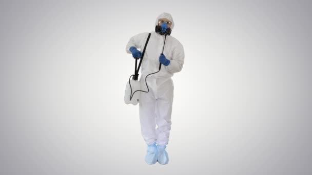 Mężczyzna w kombinezonie ochronnym i masce z środkiem dezynfekującym gotowym do pracy na gradientowym tle. — Wideo stockowe
