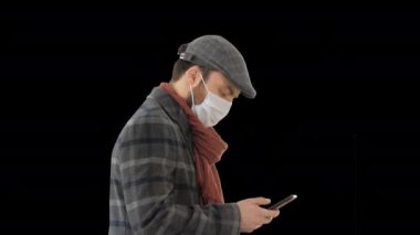 Tıbbi maskeli şık bir adam Alpha Channel 'da yürüyor ve akıllı telefon kullanıyor.