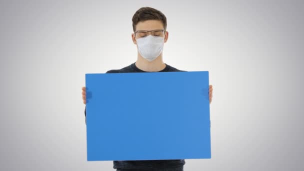 Junger Mann in medizinischer Maske zeigt und zeigt Plakat auf Gradientenhintergrund. — Stockvideo