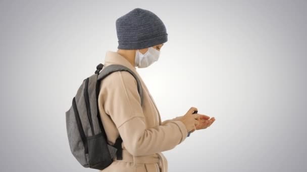 Blonde woman in medical mask during quarantine period using sanitizer on gradient background. — Stock Video