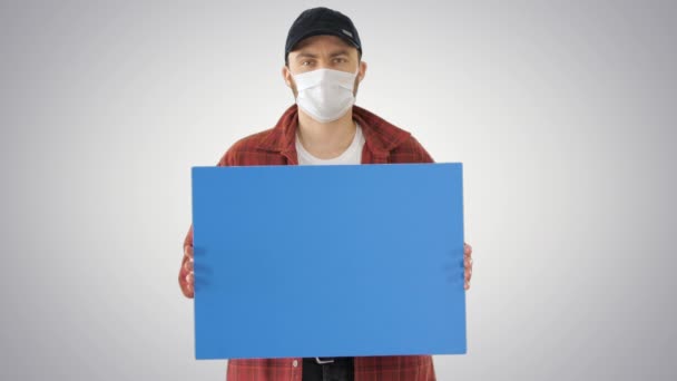 Granjero masculino maduro en máscara médica que sostiene la placa en blanco en el fondo del gradiente . — Vídeos de Stock