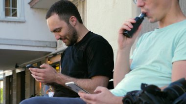 Dışarıda sigara içen bir adam başka bir adamın yanında..