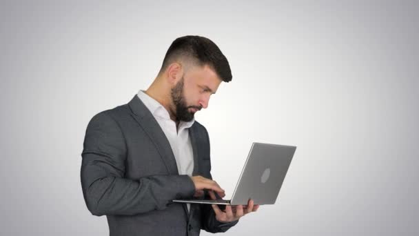 Caucásico hombre escribiendo en el ordenador portátil de pie sobre el fondo gradiente . — Vídeo de stock