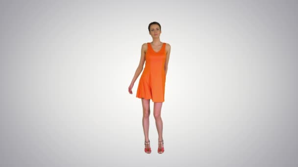 Jolie femme aux cheveux courts dansant en robe orange sur fond dégradé . — Video