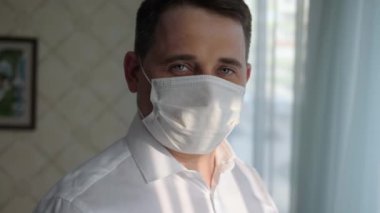 Evde kameraya bakan, tıbbi maskeli, kendine güvenen bir iş adamı..