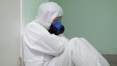 Yorgun Erkek Doktor Tehlikeli Giysiler Giyiyor Duvara Karşı Oturuyor.